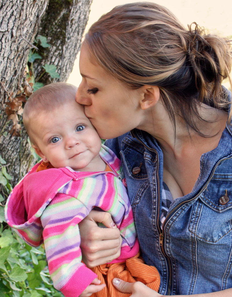 A woman kissing her baby on the cheek.