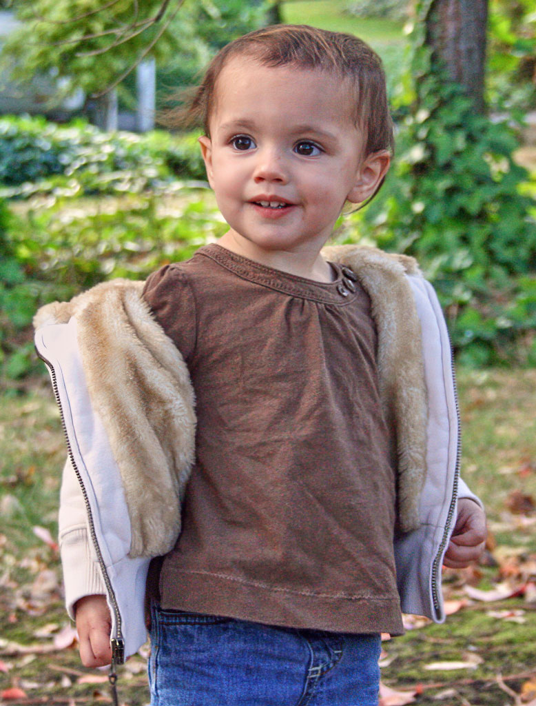 A young child wearing a brown shirt and fur vest.