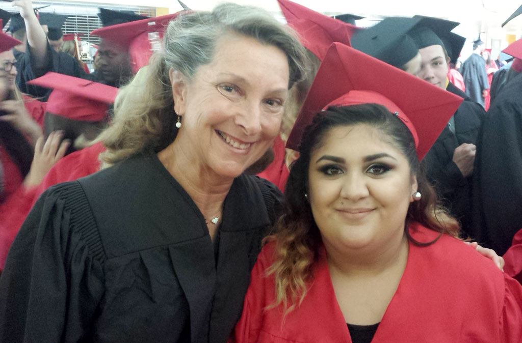 A woman and girl in graduation attire pose for the camera.