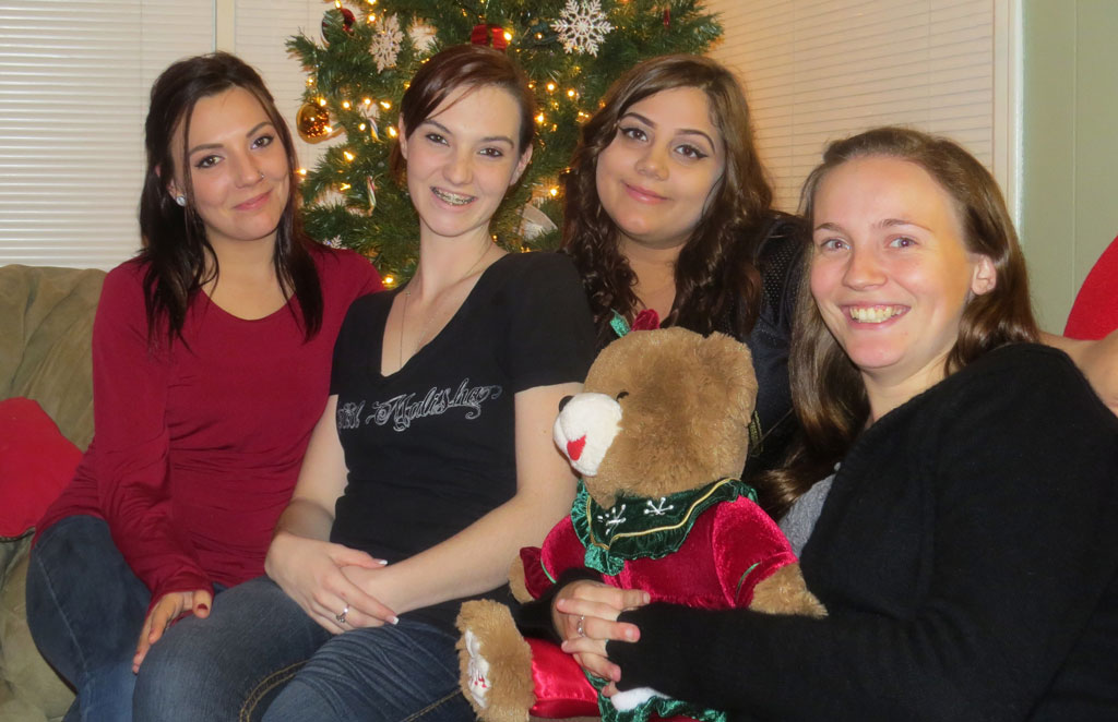 Four women sitting in front of a christmas tree.
