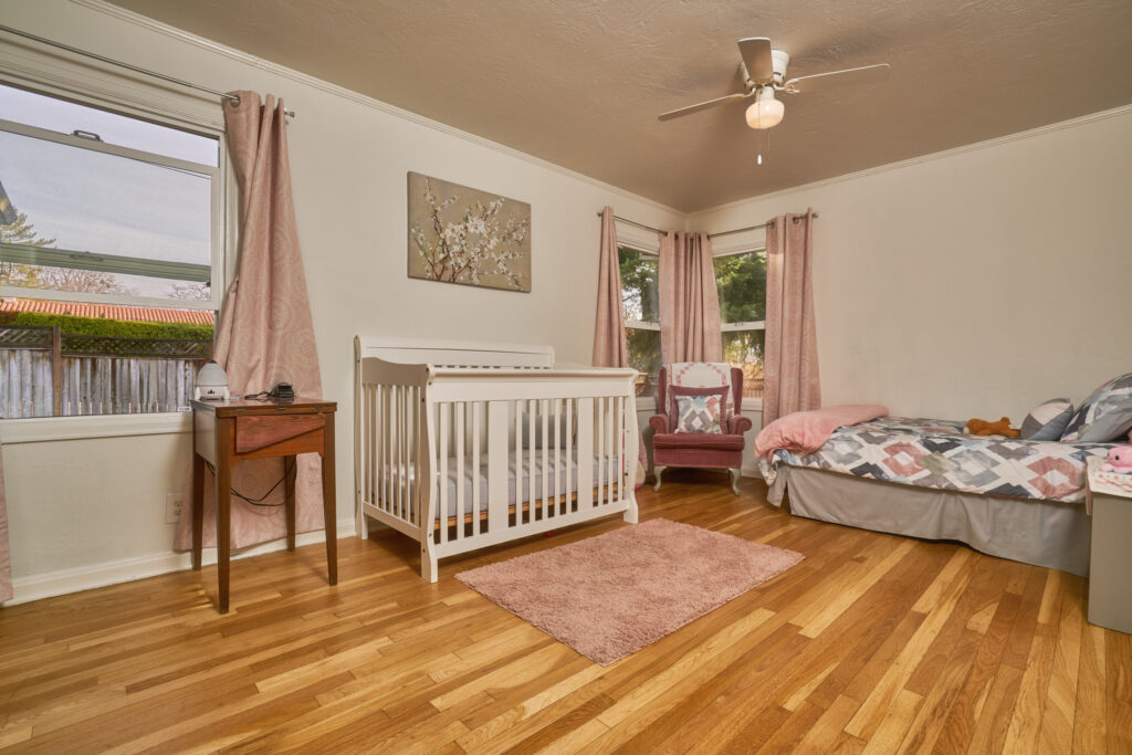 A baby room with pink curtains and wooden floors