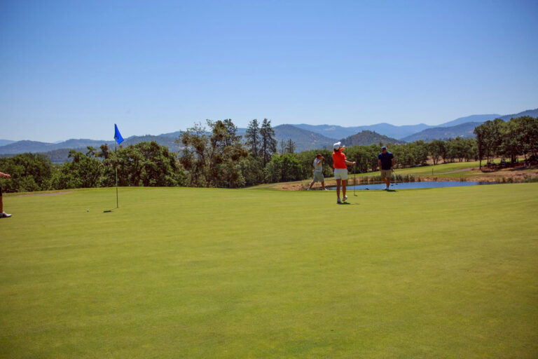 Two people playing golf on a green with mountains in the background.